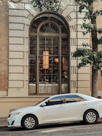 A white sedan with a freshly installed windshield gleaming under natural light in a residential street.