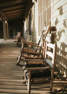 A warm photograph of an old wooden porch bathed in golden afternoon light, with weathered rocking chairs and hanging plants.