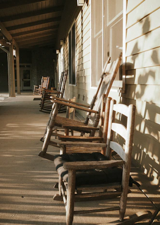 A cozy farmhouse porch with hanging herbs and a wooden rocking chair bathed in warm sunlight.