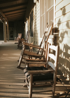 A classic wooden rocking chair on a sunlit porch with greenery.