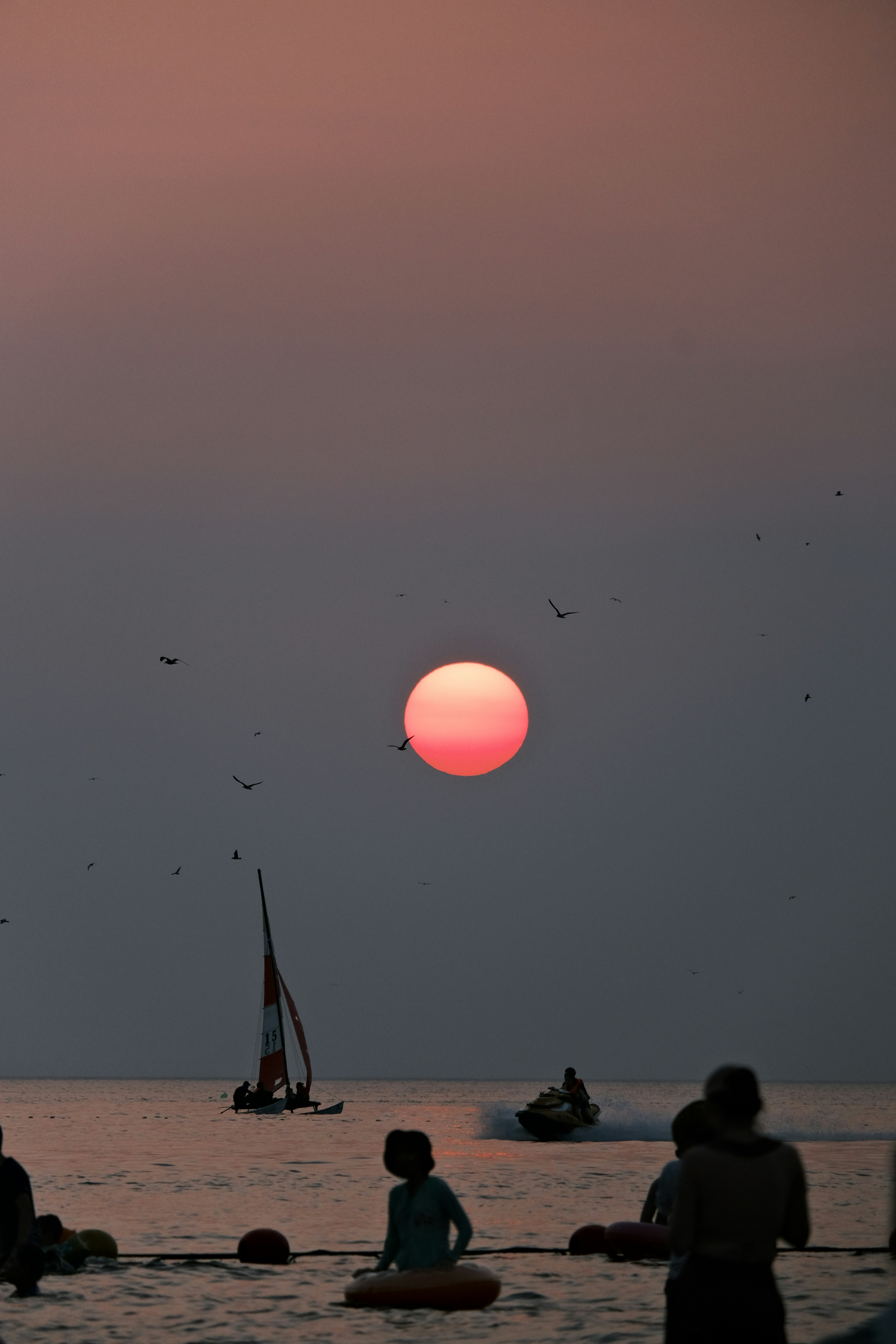 a group of people sitting on the beach watching the sun set
