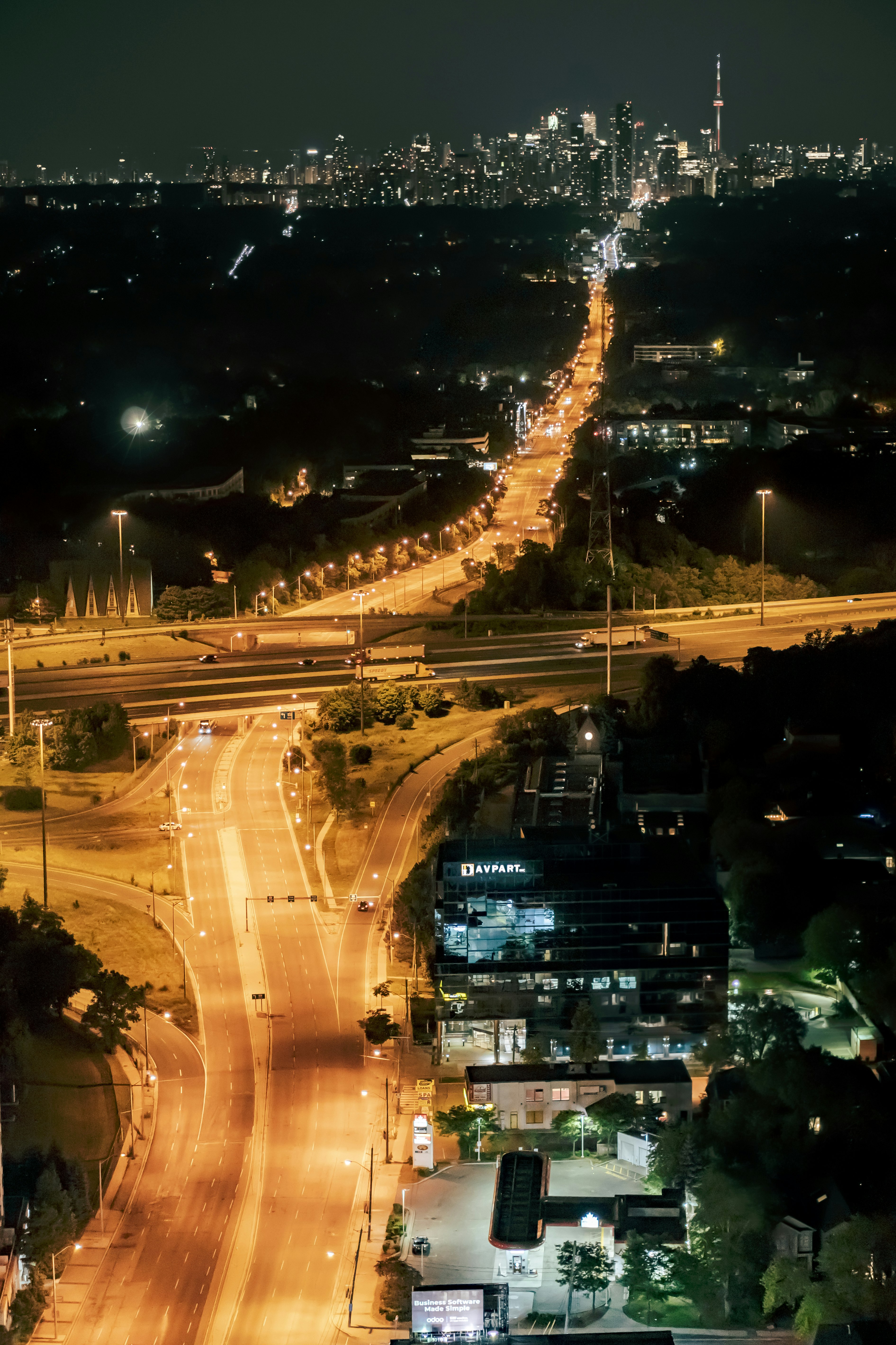 City boulevard at night with illuminated buildings, street lamps casting amber light, and the glow of a downtown skyline