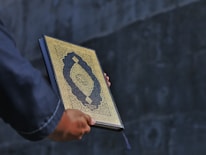Close-up of a hand holding an ancient book with dark, elegant cover.