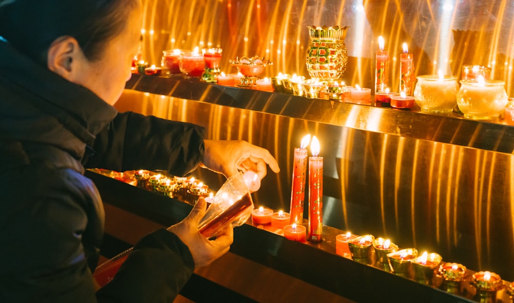 a woman lighting a candle in front of a wall of candles