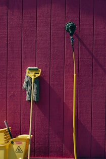a yellow mop and a yellow bucket against a pink wall