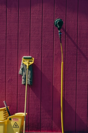 a yellow mop and a yellow bucket against a pink wall
