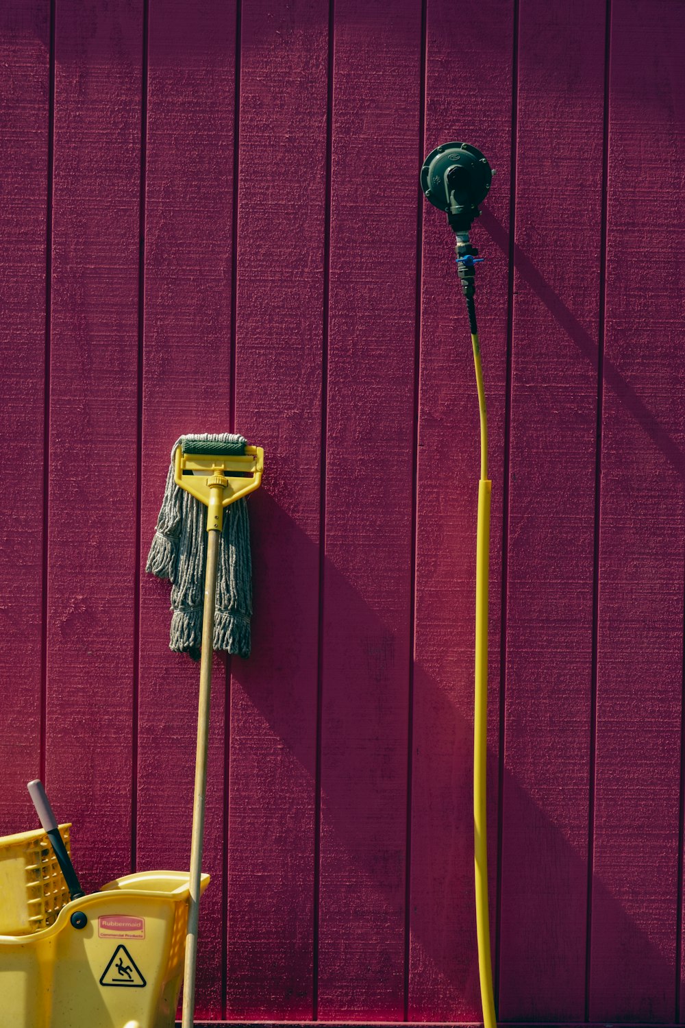 a yellow mop and a yellow bucket against a pink wall