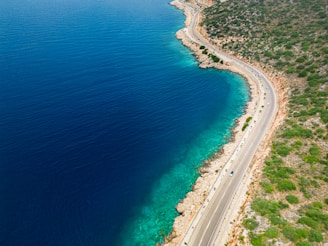 A scenic view of a coastal road with a car driving along the turquoise sea.