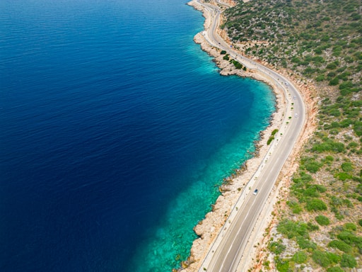 A scenic view of a coastal road with a car driving along the turquoise sea.
