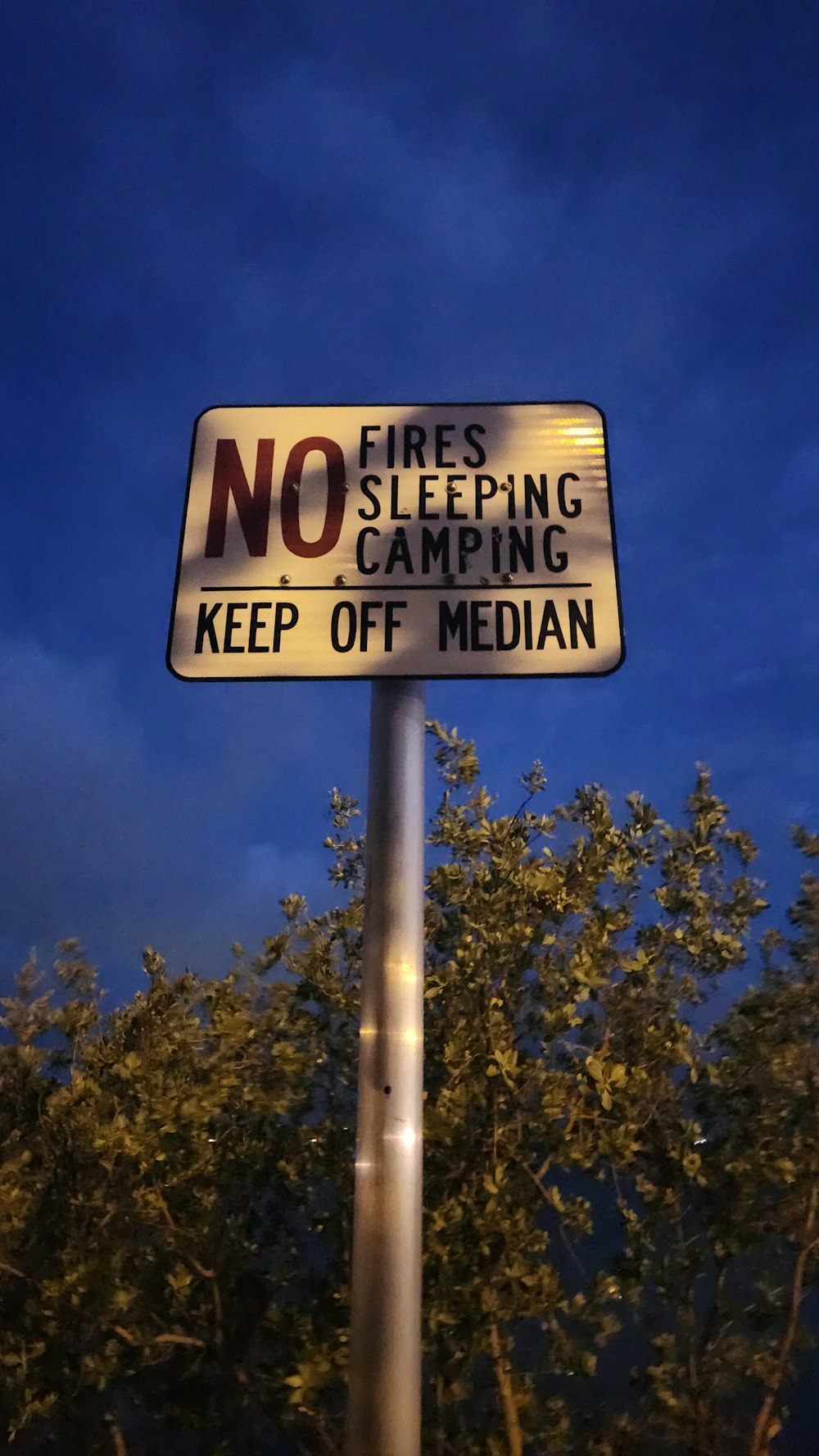 a sign on a pole that says no fire sleeping camping keep off median