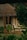 A cozy cottage with a thatched roof surrounded by lush greenery. Wooden chairs are placed on the patio, adding to the serene and rustic charm. The foliage around the house gives a natural and secluded feel.