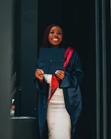 A university graduate in a blue toga and birrete holding their diploma with a big smile.