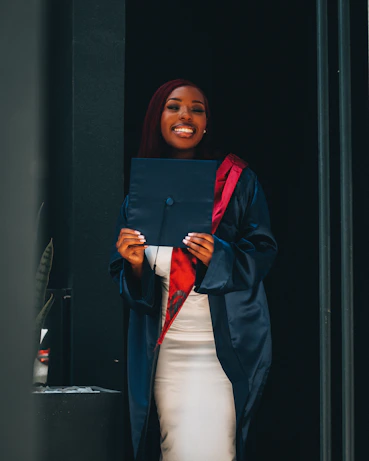 A candid moment of a graduate proudly holding their diploma, smiling brightly against a fresh teal backdrop.