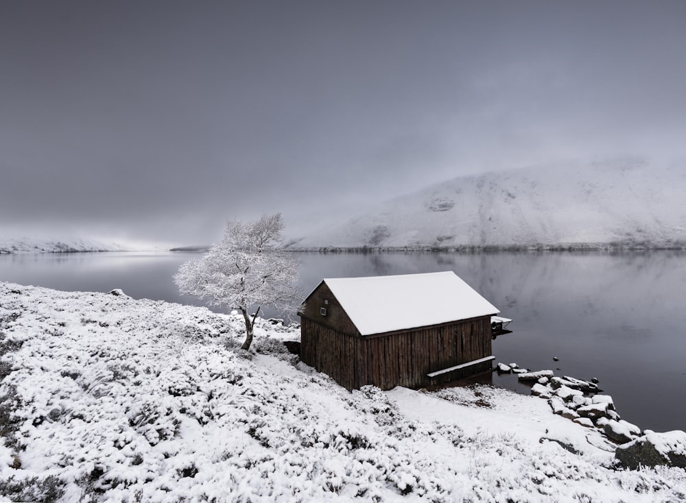 a small cabin on the shore of a lake covered in snow