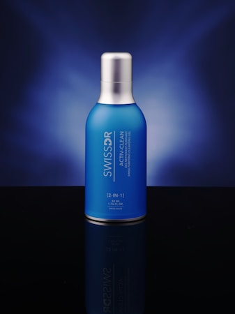 A blue bottle with a silver cap is centered against a dark blue gradient background. The bottle features white text displaying its brand and product name.