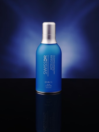 A blue bottle with a silver cap is centered against a dark blue gradient background. The bottle features white text displaying its brand and product name.