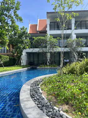Sunlit courtyard with balconies overlooking a sparkling outdoor pool surrounded by lush greenery.
