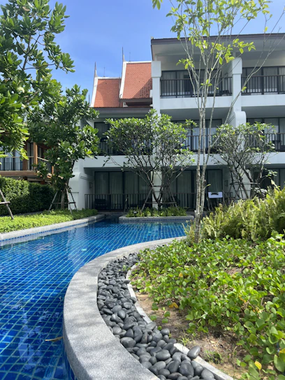 Sunlit courtyard with balconies overlooking a sparkling outdoor pool surrounded by lush greenery.