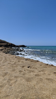 Sandy beach with natural rock pools and gentle ocean waves.