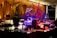 An elegant buffet setting with a variety of colorful desserts and drinks displayed on tables. Intricate sculptures, including a fish and a bird, provide decorative focal points. The ambient lighting with warm tones adds sophistication to the atmosphere.