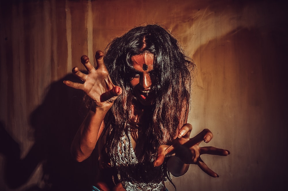 a woman with long hair and makeup holding her hands up