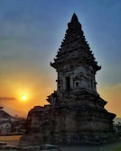 An ancient temple silhouetted against a fiery sunset with intricate carvings visible.