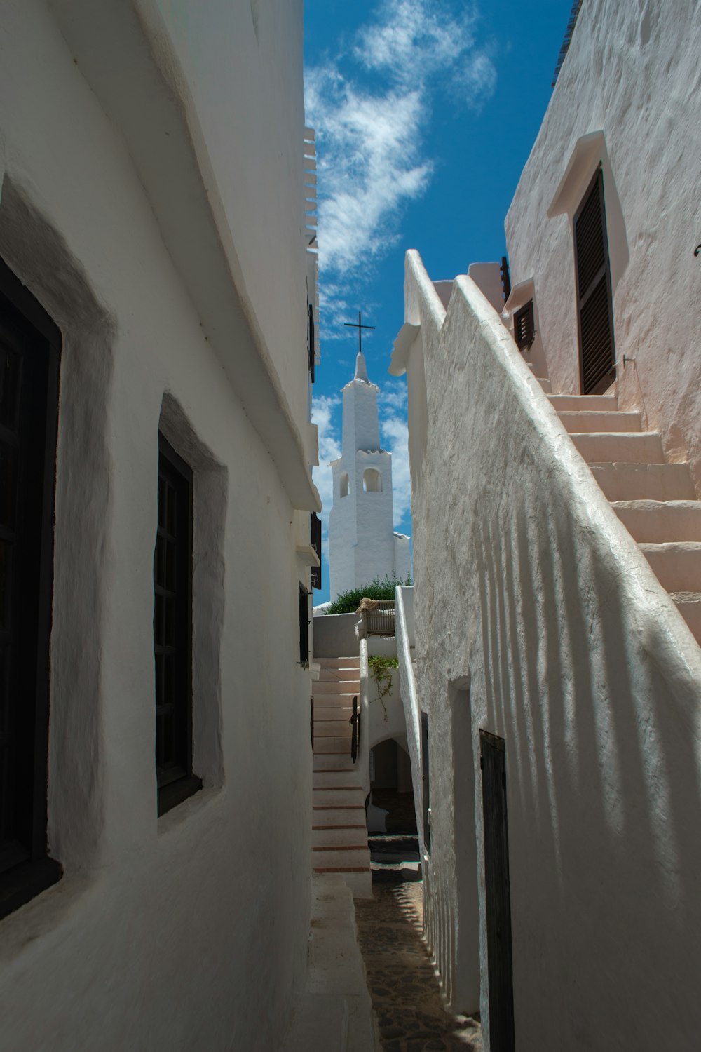 Un callejón estrecho con edificios blancos y un campanario en el fondo