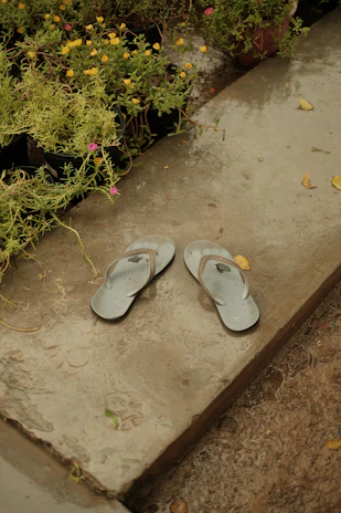 A pair of soft, gray non-slip slippers resting on a bathroom floor with water droplets nearby.