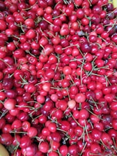 A large quantity of bright red cherries with green stems, closely packed together. The cherries are fresh and glossy, indicating ripeness and quality.