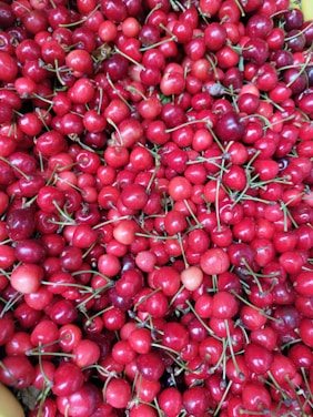 A large quantity of bright red cherries with green stems, closely packed together. The cherries are fresh and glossy, indicating ripeness and quality.