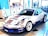 A sleek, white sports car decorated with various sponsor logos on its body. It's displayed in an indoor setting with a modern almost minimalist interior, including blue and white walls, large windows, and promotional banners in the background.