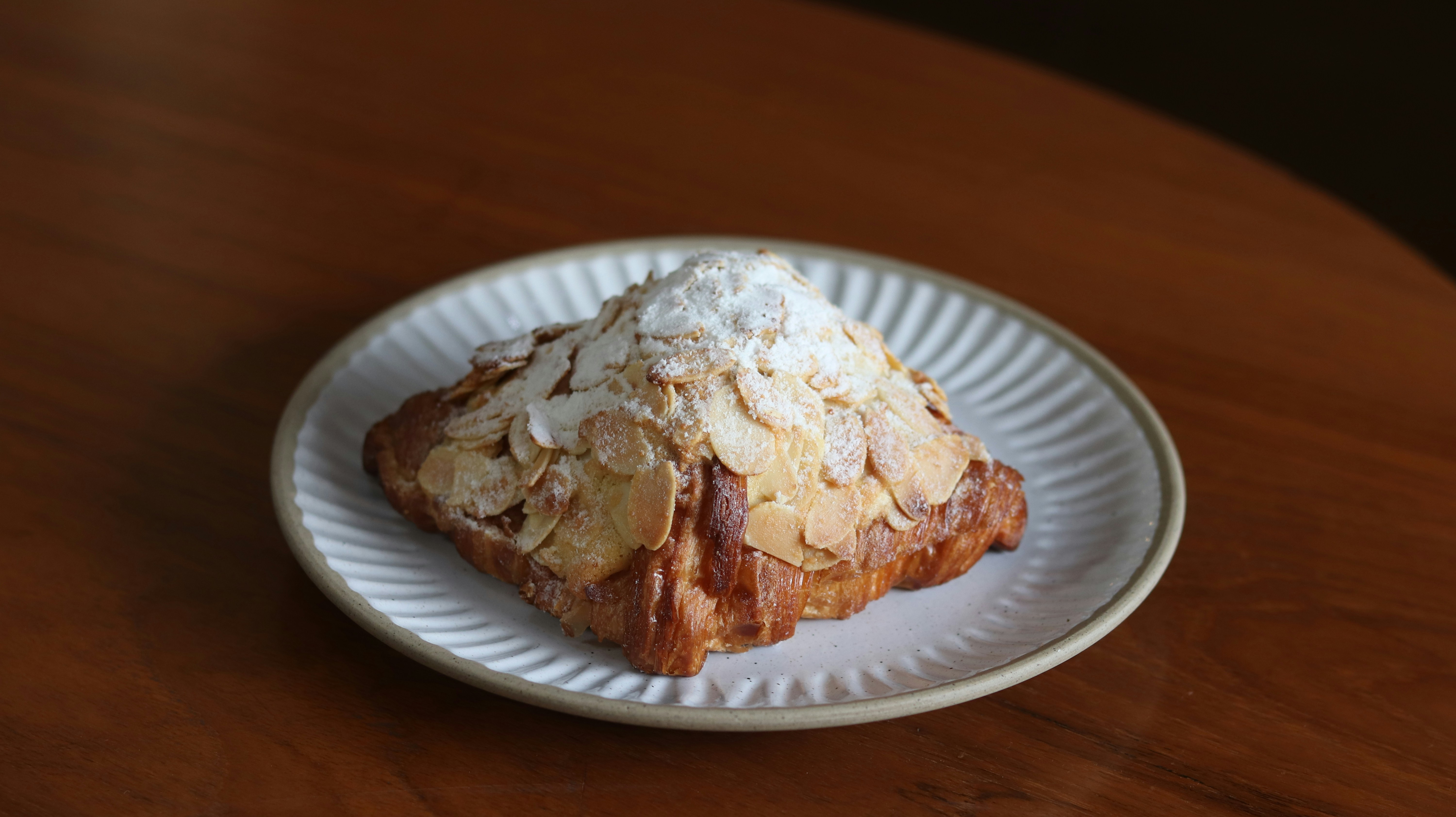 Almond croissant with toasted almond flakes on top, powdered sugar dusting, white plate