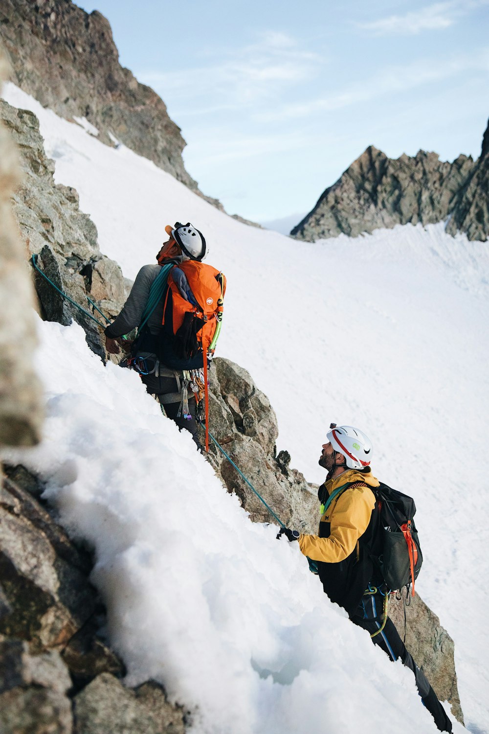 a couple of people climbing up the side of a snow covered mountain