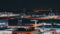 A nighttime shot of an illuminated control tower overseeing a busy airport apron.