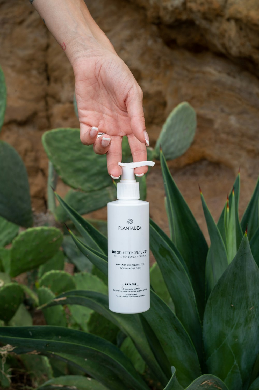 a person holding a bottle of hand sanitizer in front of a plant