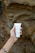 A hand with a tattoo on the wrist is holding a tube of hand cream labeled 'PLANTADEA BIO CREMA MANI' against a textured rocky background.