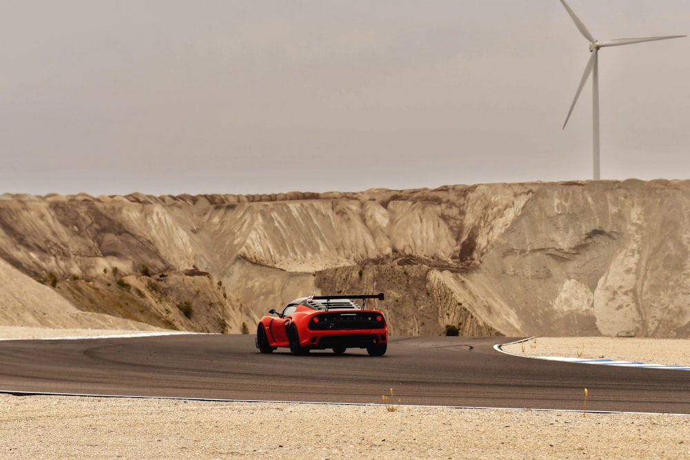 Un'auto sportiva rossa che guida lungo una strada vicino a una turbina eolica