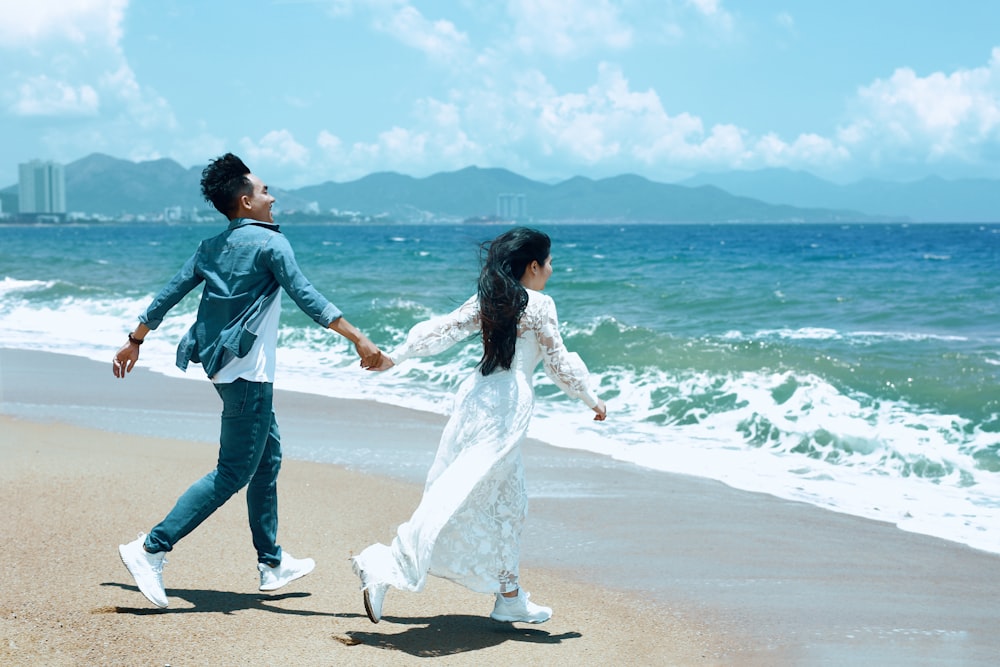 a man and a woman holding hands while walking on the beach