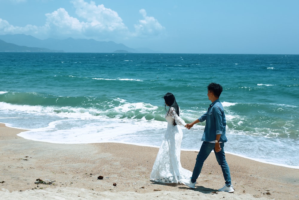 a bride and groom walking on the beach holding hands