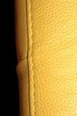 A close-up view of a textured yellow leather surface, displaying visible stitching along a seam. The background is dark, enhancing the texture and color of the leather.