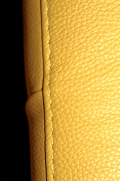 A close-up view of a textured yellow leather surface, displaying visible stitching along a seam. The background is dark, enhancing the texture and color of the leather.