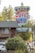 A colorful motel sign with a crown design advertising the Crown Motel with private beach access and no vacancy. Below it is another sign indicating Lakefront Lodging. The background features a building with a balcony, surrounded by trees and parked vehicles. The environment suggests a serene, natural setting.