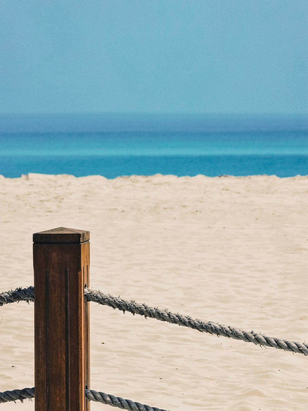 a wooden post on a beach next to a rope fence