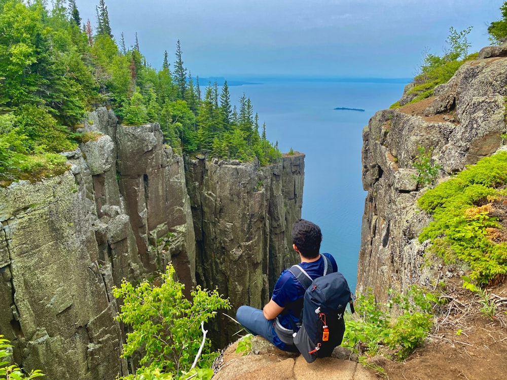 a man sitting on top of a cliff overlooking a body of water