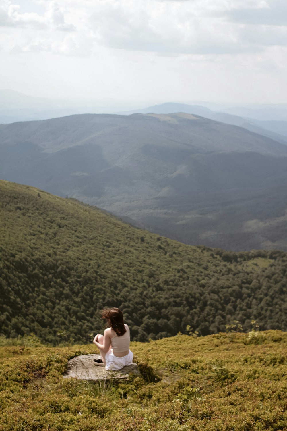 a woman sitting on top of a lush green hillside