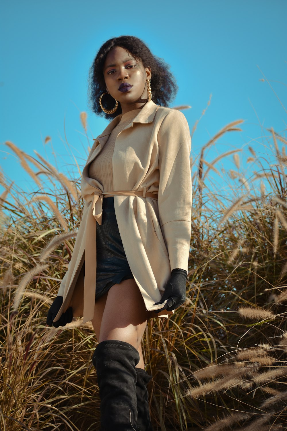 a woman standing in tall grass wearing a trench coat