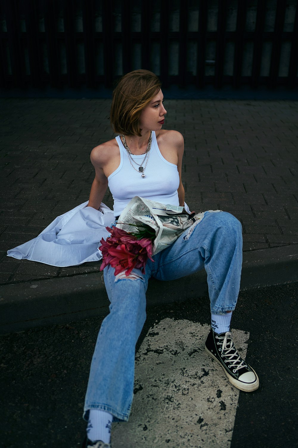 a woman sitting on a curb with a bouquet of flowers