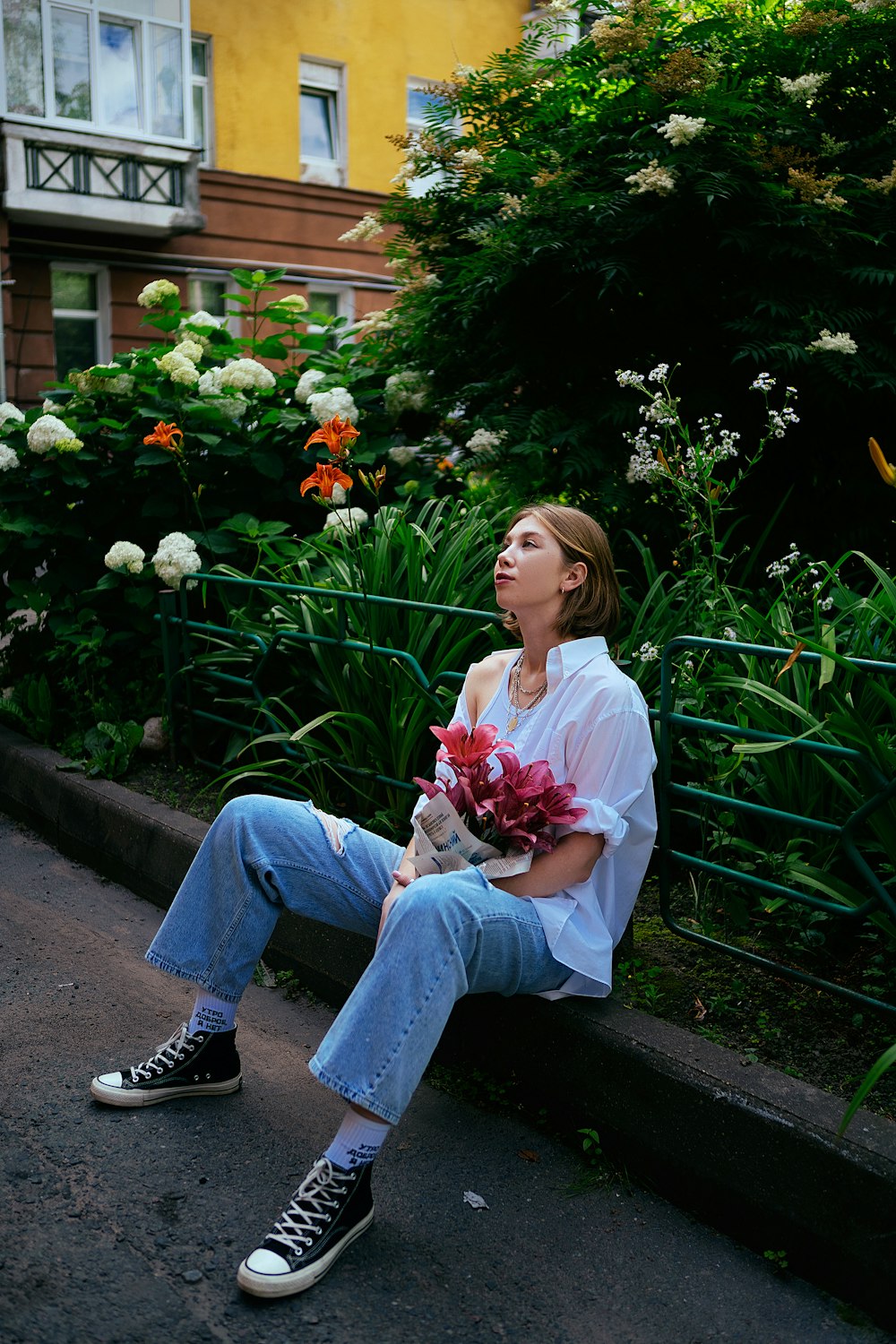 a woman sitting on a curb holding a bouquet of flowers