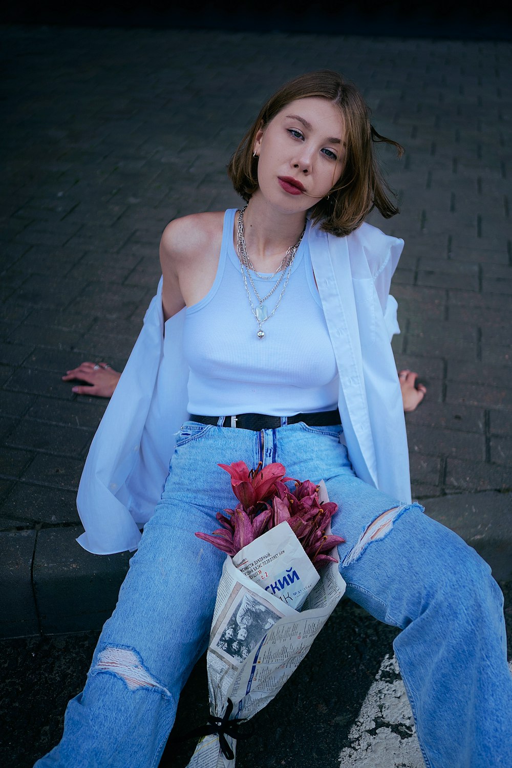 a woman sitting on a curb with a bag of flowers