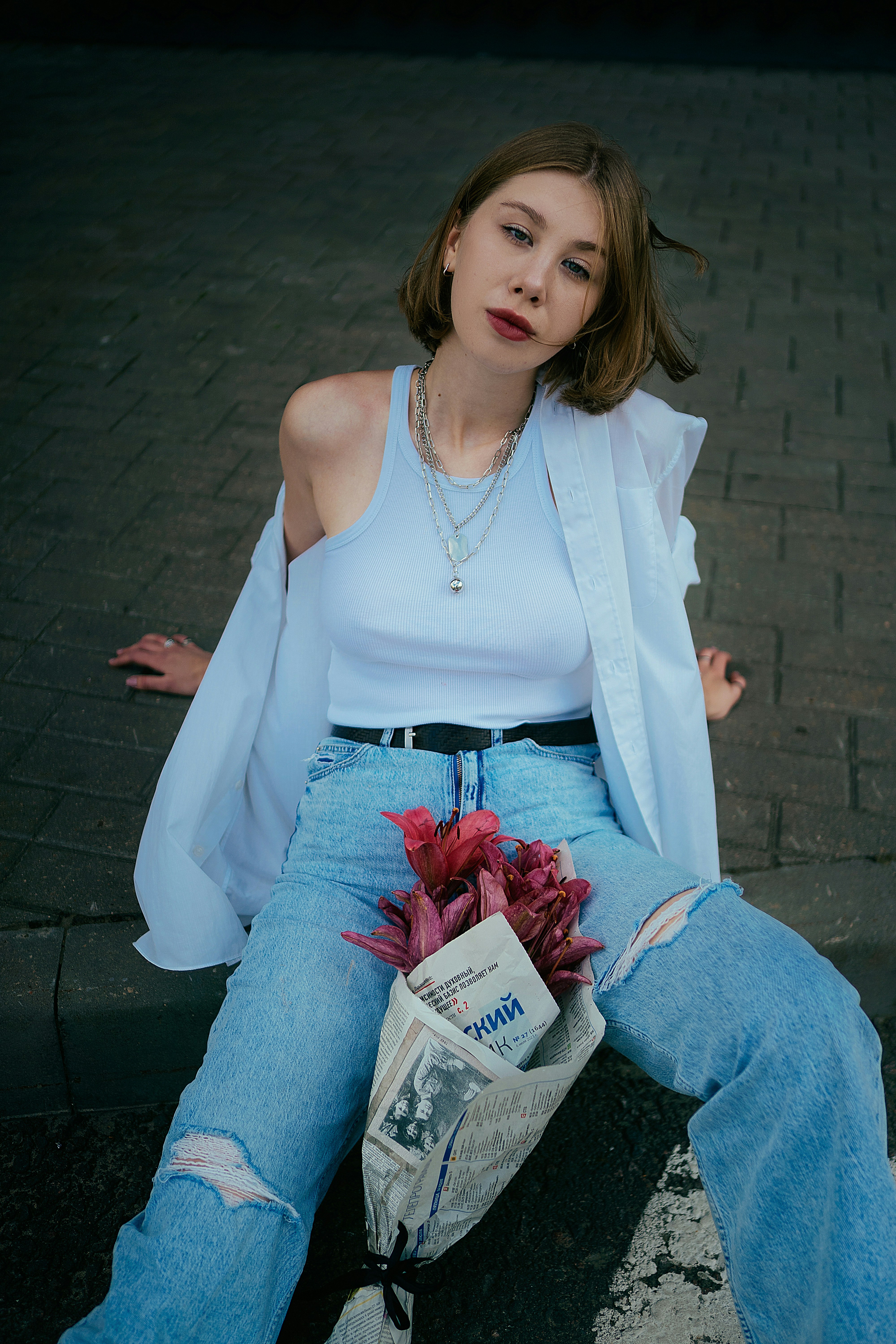 a woman sitting on a curb with a bag of flowers